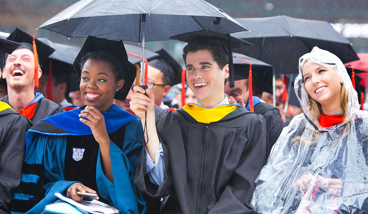 Graduates smiling as they sit at commencement in the rain