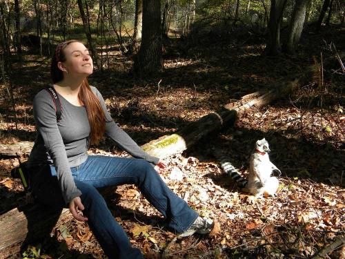 Lydia Greene sits on a log in the woods next to a lemur.