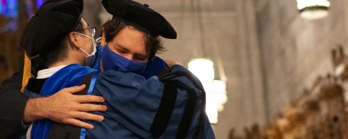 Adviser and graduate exchange a hug after hooding