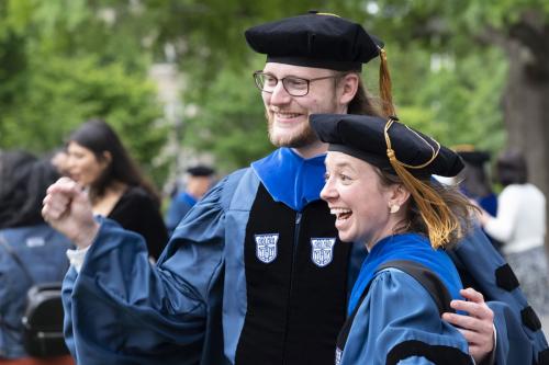 Two students celebrate while posing for picture after hooding