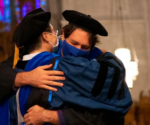 Student and advisor exchange a hug at the hooding ceremony
