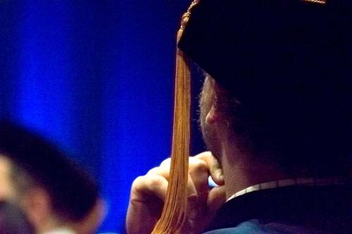 Shot of back of graduate looking into the distance with chin resting on hand at hooding ceremony
