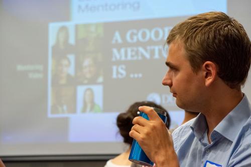 Student looks left while the screen behind him shows "A Good Mentor Is ..."