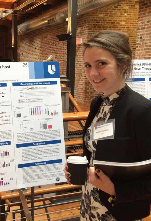 Photo of Caitlin Murdoch posing next to her thesis presentation.